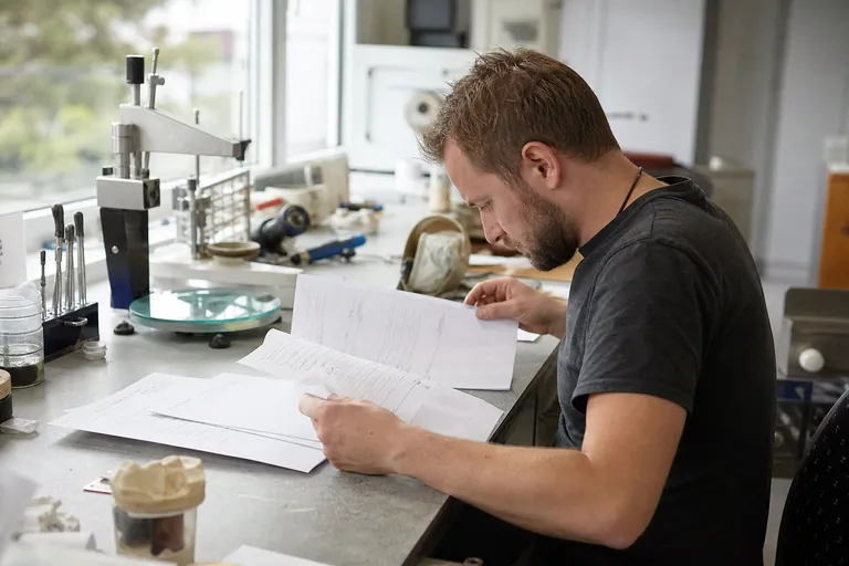 Zahntechniker sucht in Lieferscheinen nach einer Chargenangabe für einen Arbeitsauftrag.