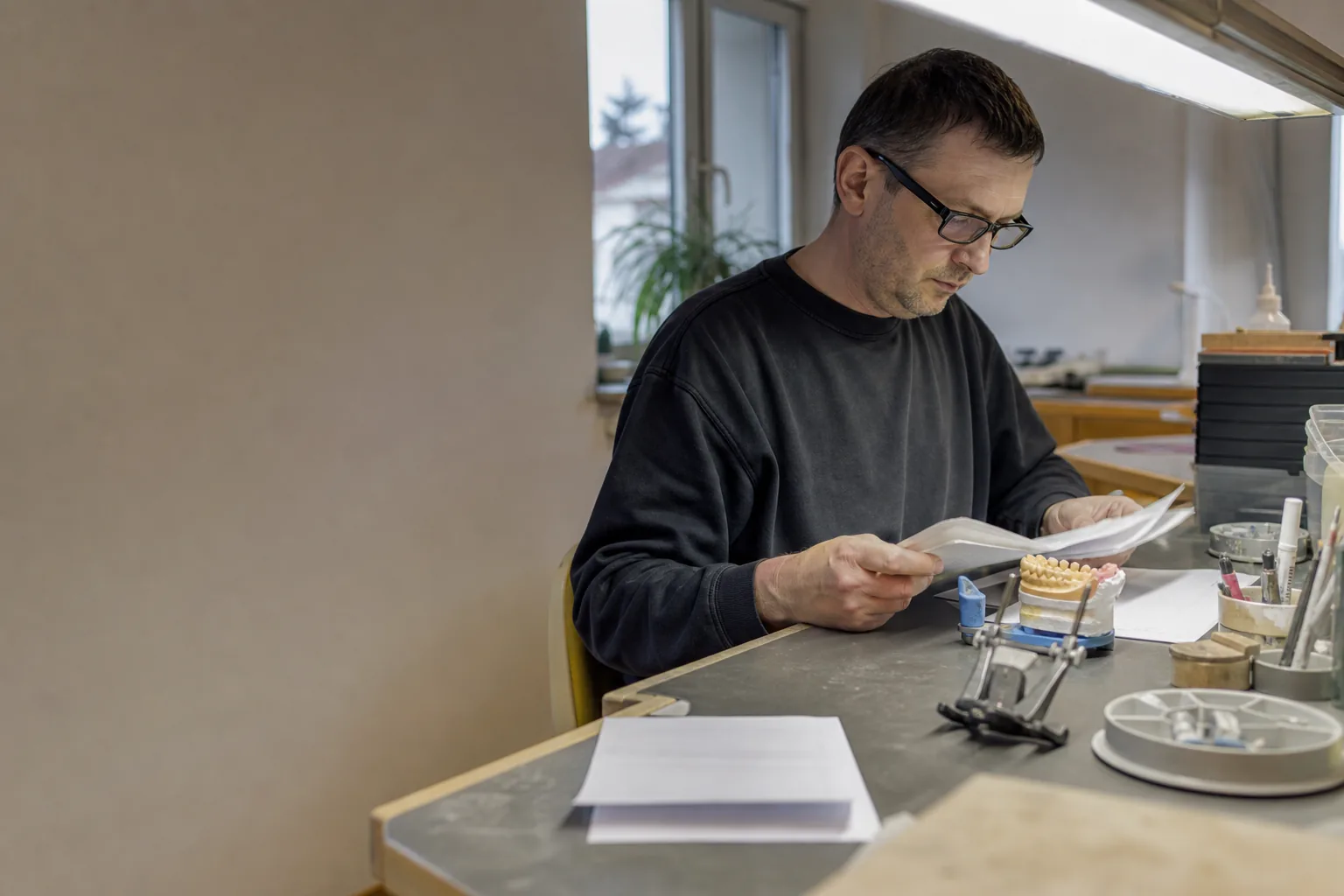 Zahntechniker prüft am Arbeitsplatz einen Auftrag und einen Materiallieferschein