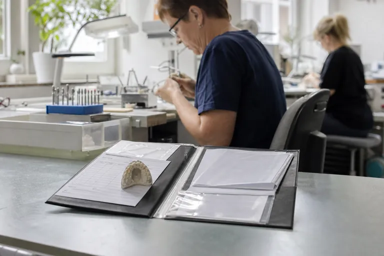 Dokumentenmappe mit Werkstückauftrag, Materialetiketten und Lieferscheinen auf einem Labortisch.
