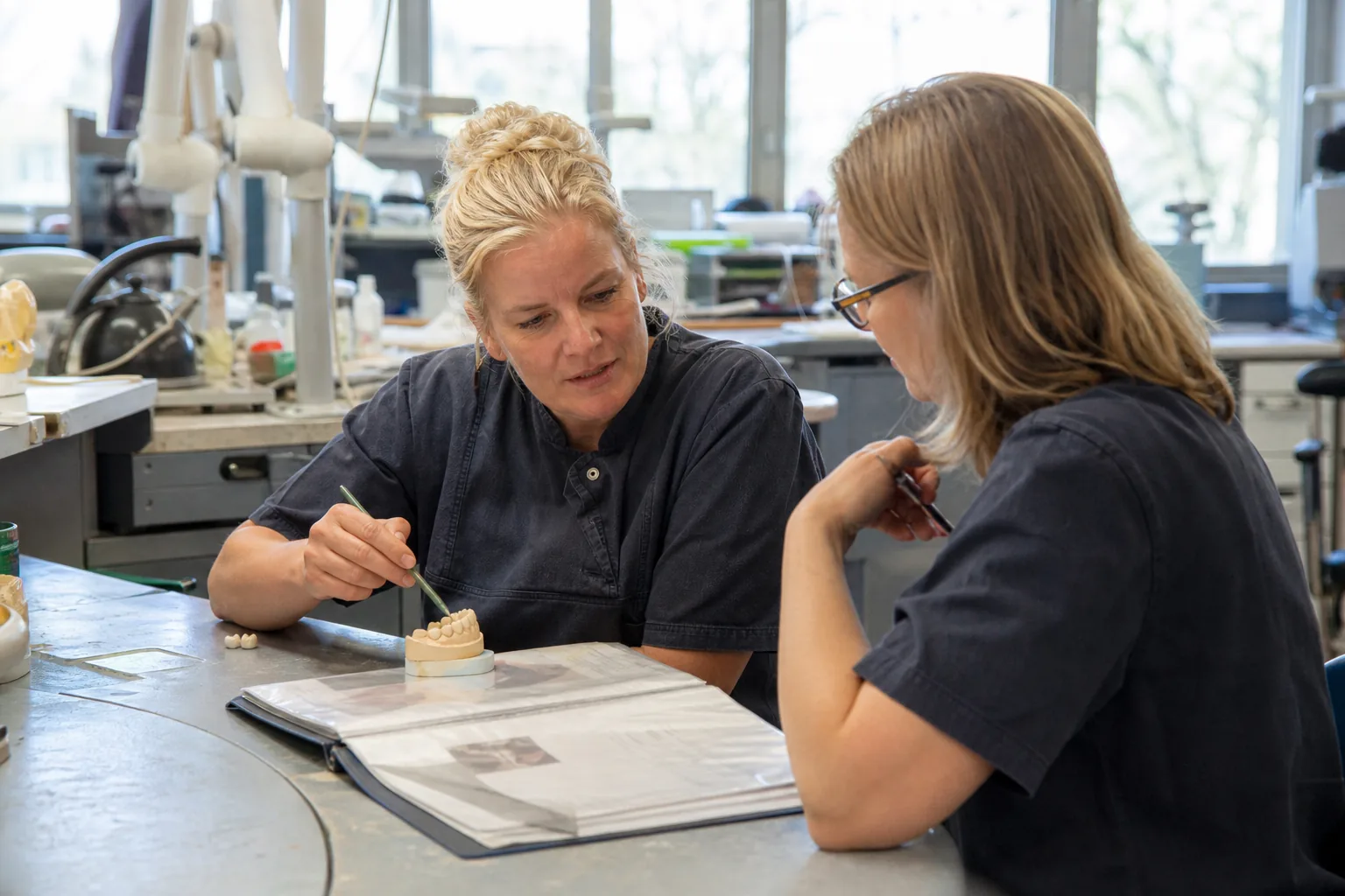 Meisterin und Kollegin im Dentallabor besprechen einen Werkstückauftrag neben einem Modell.